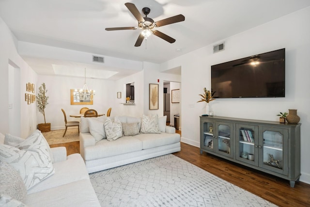 living room featuring ceiling fan with notable chandelier, a raised ceiling, and dark wood-type flooring