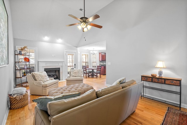 living room featuring ceiling fan with notable chandelier, light hardwood / wood-style flooring, and high vaulted ceiling