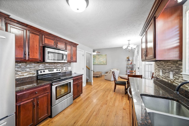 kitchen featuring sink, light hardwood / wood-style flooring, decorative backsplash, dark stone countertops, and appliances with stainless steel finishes