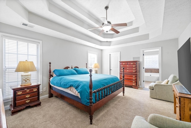 carpeted bedroom featuring a raised ceiling, ensuite bath, ceiling fan, a textured ceiling, and multiple windows