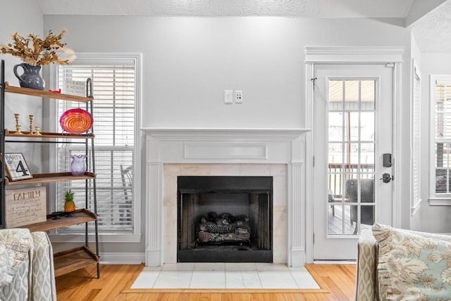 living room with a tile fireplace, a textured ceiling, and light wood-type flooring