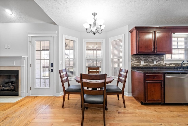 dining area with a notable chandelier, light wood-type flooring, a textured ceiling, and a tile fireplace