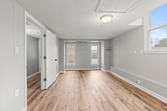 empty room with a textured ceiling, light wood finished floors, and baseboards