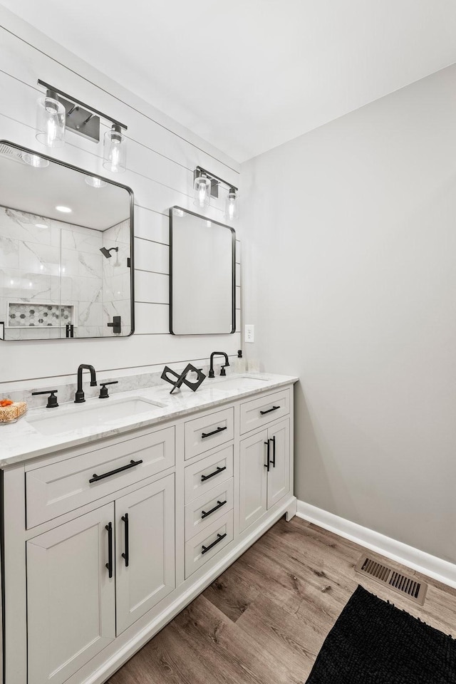 bathroom featuring visible vents, a sink, a marble finish shower, and wood finished floors