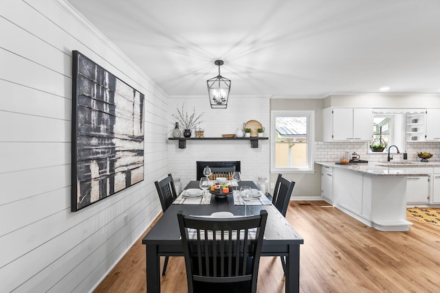 dining room featuring light wood finished floors, wooden walls, ornamental molding, and an inviting chandelier