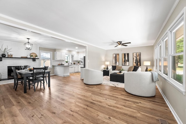 living room with ceiling fan with notable chandelier, light hardwood / wood-style floors, ornamental molding, and a wealth of natural light