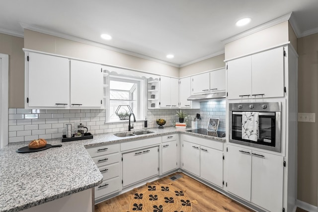 kitchen with white cabinets, stainless steel oven, a sink, under cabinet range hood, and black electric cooktop