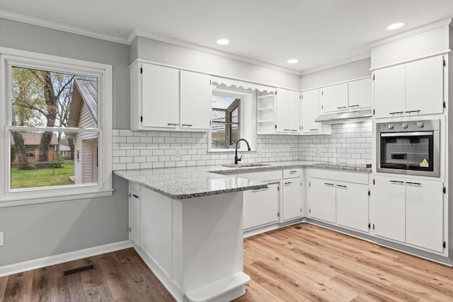 kitchen with stainless steel oven, light stone countertops, under cabinet range hood, white cabinetry, and a sink