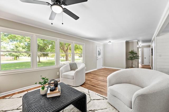 living room with light wood finished floors, a ceiling fan, baseboards, and crown molding