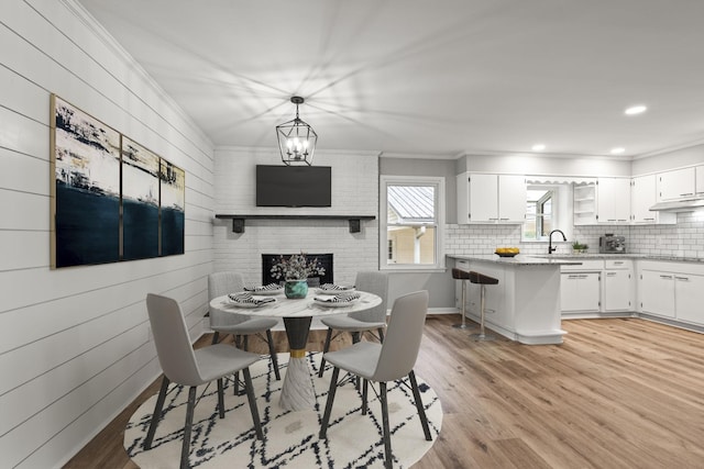 dining room featuring a fireplace, crown molding, recessed lighting, an inviting chandelier, and light wood-style floors