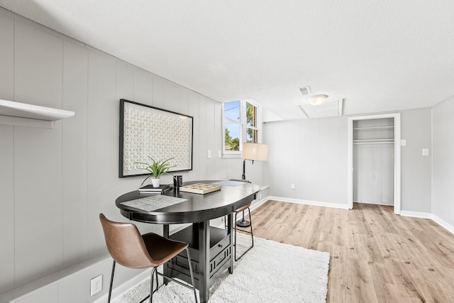 dining space with light wood-type flooring, visible vents, a textured ceiling, and baseboards