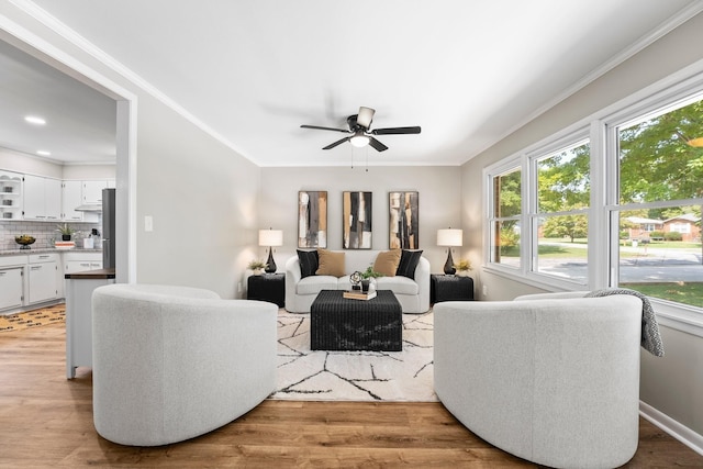 living room with light wood-type flooring, baseboards, a ceiling fan, and crown molding