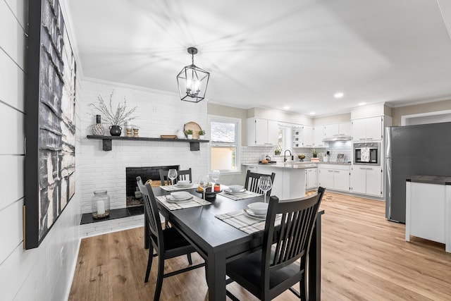 dining area featuring light wood-style floors, a fireplace, crown molding, and brick wall