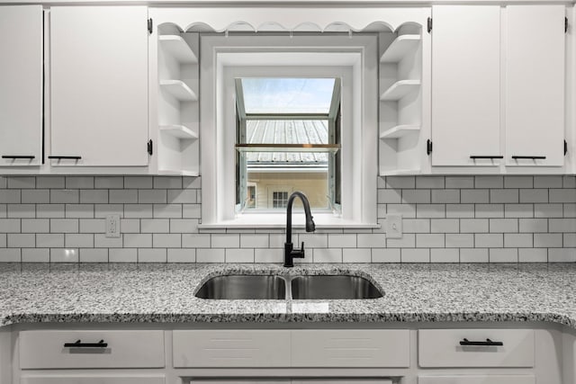 kitchen with light stone countertops, white cabinetry, open shelves, and a sink