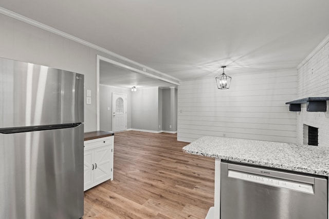 kitchen featuring pendant lighting, appliances with stainless steel finishes, light wood-style floors, ornamental molding, and white cabinetry