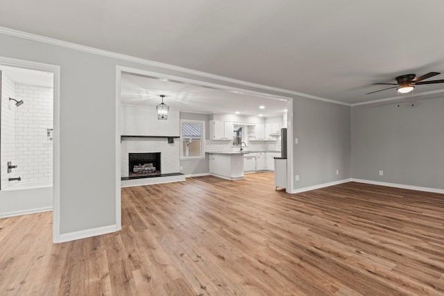 unfurnished living room featuring baseboards, ornamental molding, a brick fireplace, and light wood-style floors