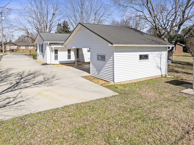 view of property exterior with metal roof, driveway, and a lawn