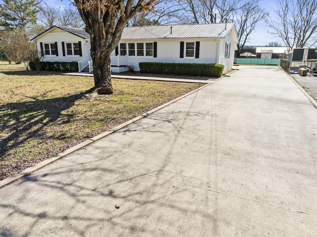 ranch-style house with driveway, metal roof, fence, a front lawn, and brick siding