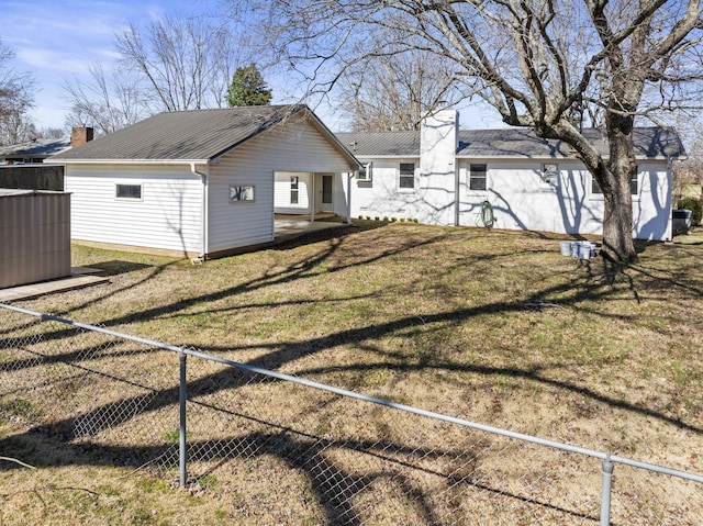 back of house featuring a chimney, fence, metal roof, and a yard