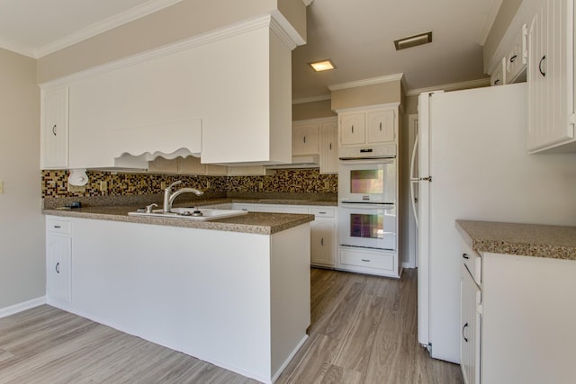 kitchen with white appliances, kitchen peninsula, sink, and white cabinets