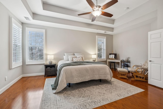 bedroom featuring multiple windows, hardwood / wood-style floors, a tray ceiling, and ceiling fan