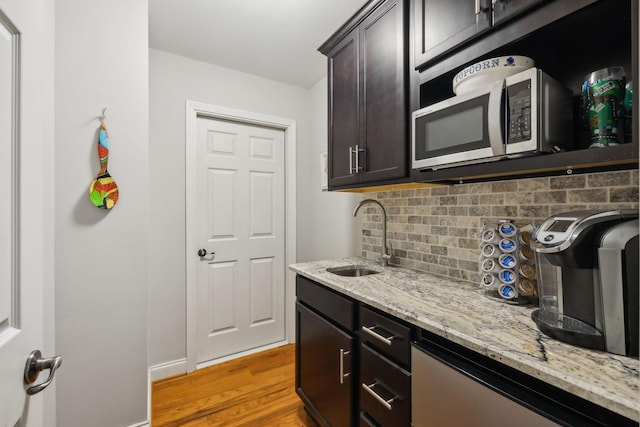 kitchen with decorative backsplash, light stone counters, dark brown cabinetry, sink, and light hardwood / wood-style flooring