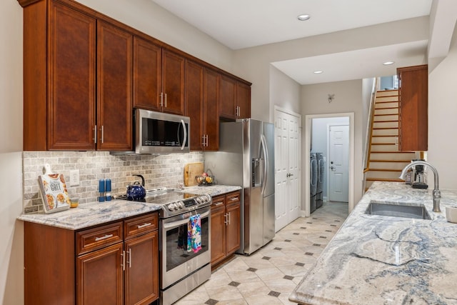 kitchen with light stone countertops, tasteful backsplash, stainless steel appliances, sink, and independent washer and dryer