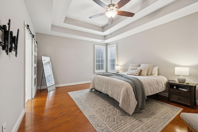 bedroom with hardwood / wood-style floors, a barn door, a raised ceiling, and ceiling fan