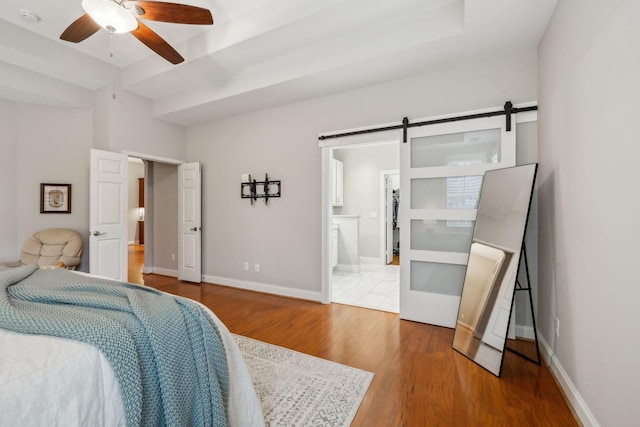 bedroom with a barn door, ensuite bathroom, ceiling fan, and wood-type flooring