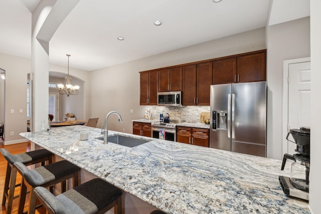 kitchen featuring an inviting chandelier, sink, light stone countertops, appliances with stainless steel finishes, and tasteful backsplash