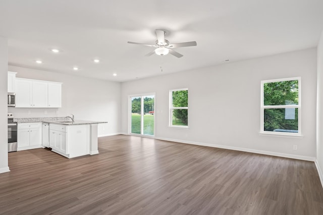 unfurnished living room featuring a healthy amount of sunlight, ceiling fan, dark wood-type flooring, and sink