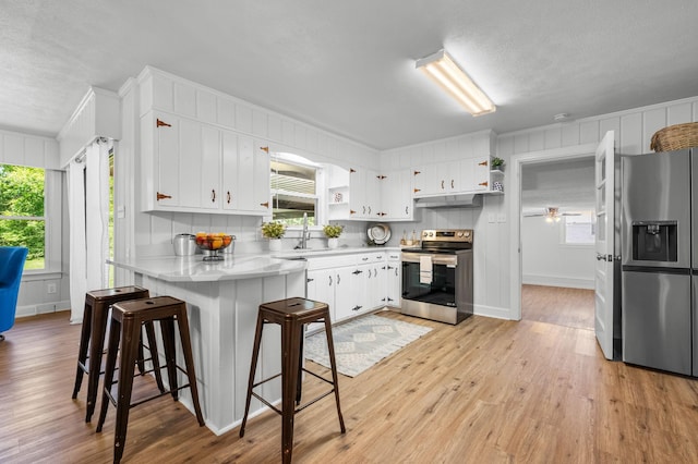 kitchen featuring kitchen peninsula, a breakfast bar, stainless steel appliances, light hardwood / wood-style flooring, and white cabinets