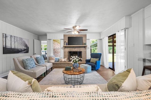 living room featuring ceiling fan, a healthy amount of sunlight, dark hardwood / wood-style flooring, and a brick fireplace