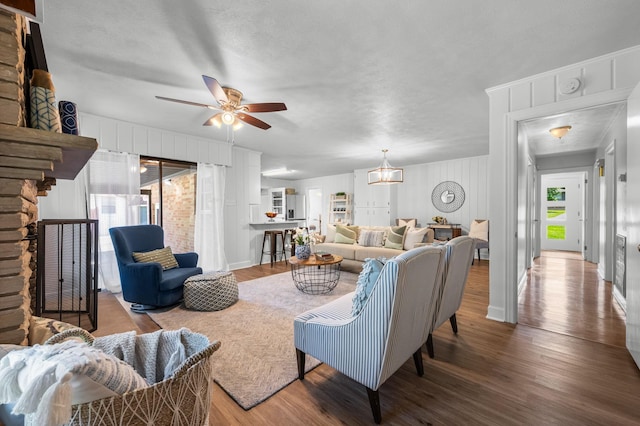 living room with hardwood / wood-style floors, ceiling fan with notable chandelier, a stone fireplace, and a wealth of natural light