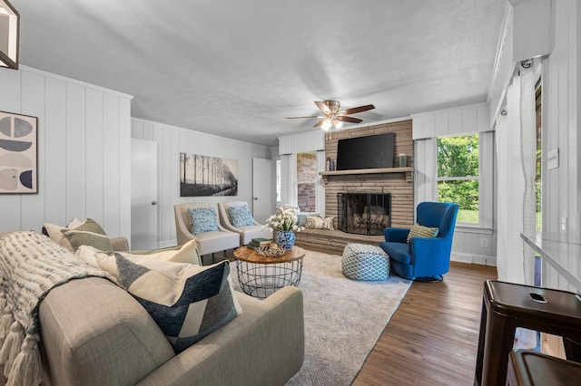 living room with dark hardwood / wood-style flooring, a stone fireplace, ceiling fan, and wood walls