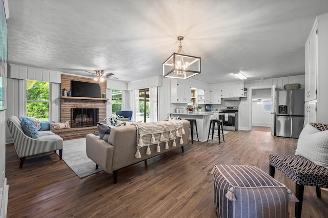 living room featuring a textured ceiling, a fireplace, dark wood-type flooring, and ceiling fan with notable chandelier