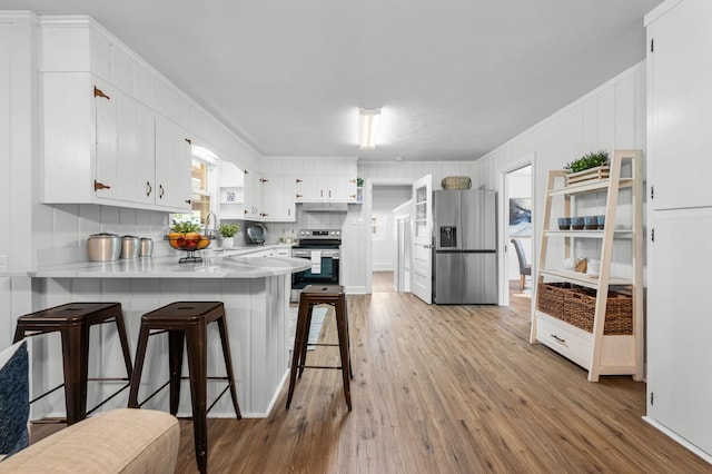 kitchen featuring sink, white cabinetry, light hardwood / wood-style floors, kitchen peninsula, and stainless steel appliances