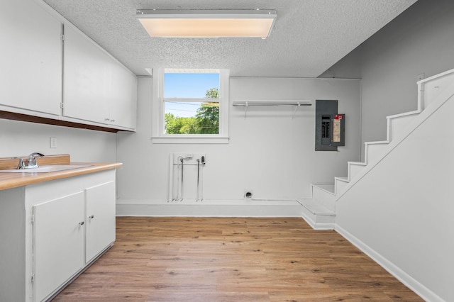 laundry room featuring a textured ceiling, cabinets, sink, and electric panel