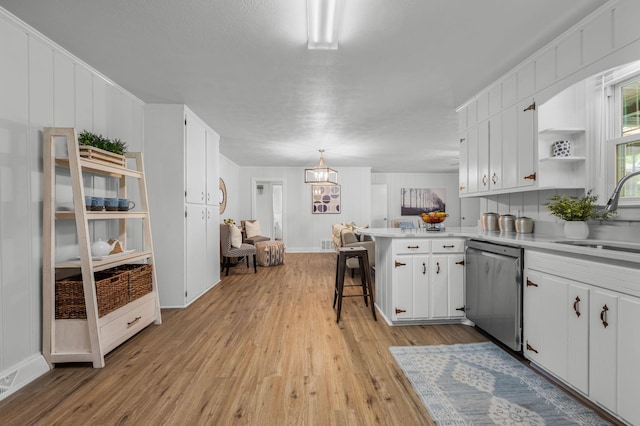 kitchen with white cabinetry, dishwasher, sink, kitchen peninsula, and a kitchen bar