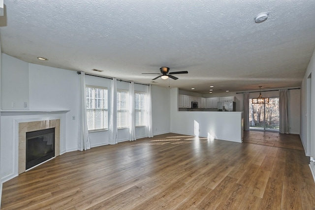 unfurnished living room with hardwood / wood-style floors, ceiling fan, a textured ceiling, and a tiled fireplace