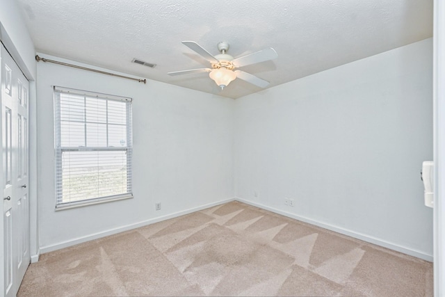 empty room with ceiling fan, light colored carpet, and a textured ceiling