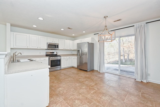 kitchen with appliances with stainless steel finishes, sink, pendant lighting, a notable chandelier, and white cabinets