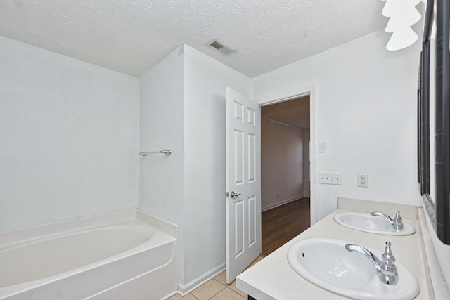 bathroom with tile patterned floors, a tub, vanity, and a textured ceiling