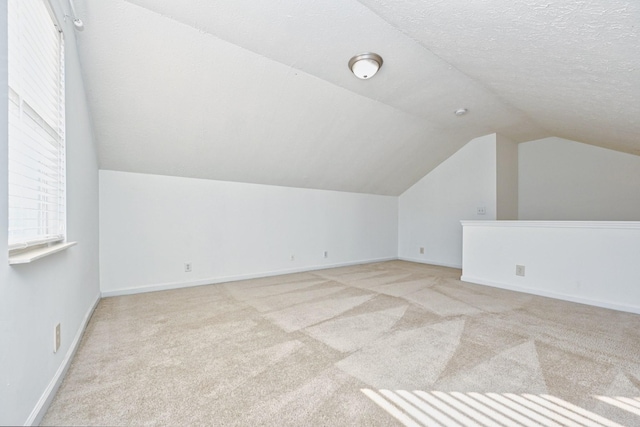 additional living space with lofted ceiling, light carpet, and a textured ceiling