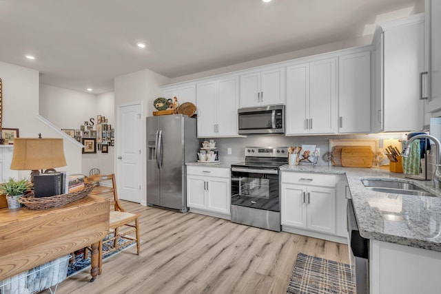 kitchen featuring sink, light wood-type flooring, light stone countertops, appliances with stainless steel finishes, and white cabinetry