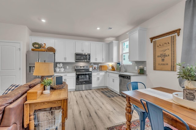 kitchen with white cabinetry, sink, stainless steel appliances, and light hardwood / wood-style floors