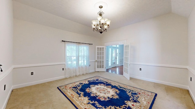 empty room with french doors, carpet floors, an inviting chandelier, and vaulted ceiling