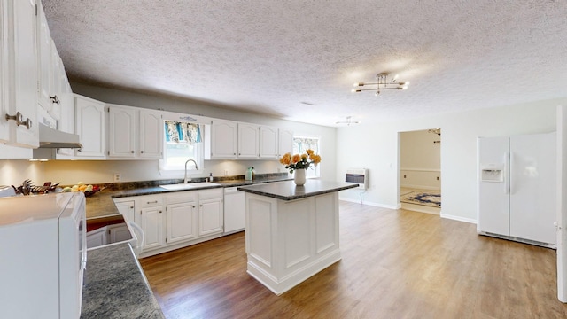 kitchen with white cabinetry, sink, a center island, heating unit, and white appliances