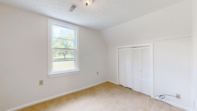 unfurnished bedroom featuring a textured ceiling, a closet, carpet, and lofted ceiling