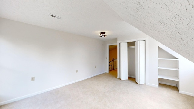 unfurnished bedroom featuring a textured ceiling, light colored carpet, and vaulted ceiling